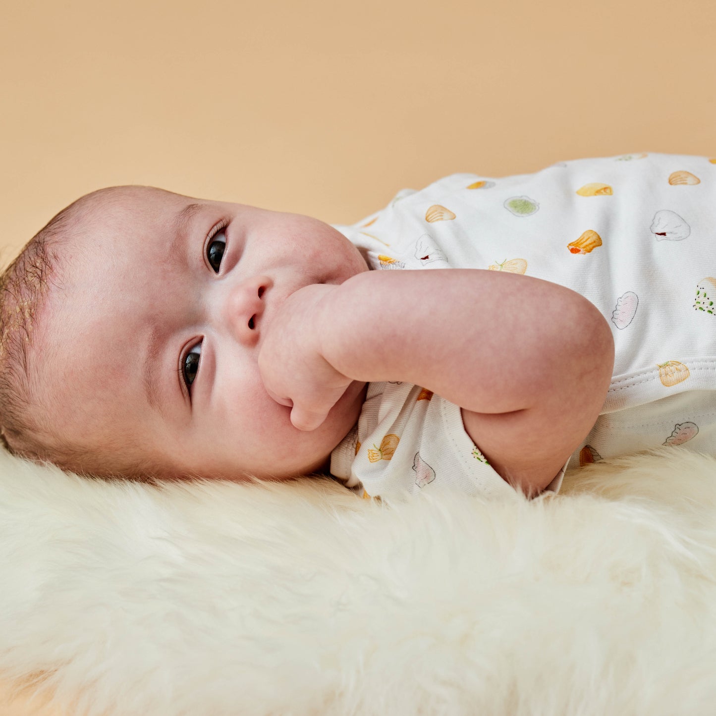 Baby with dim sum inspired baby bodysuit and sucking his fist